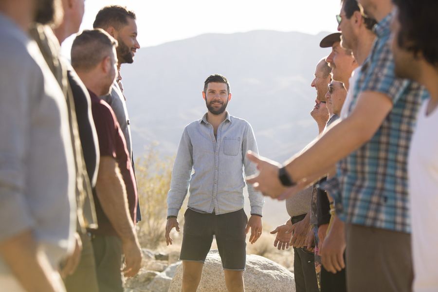 Travis standing among a circle of men on a mountainside