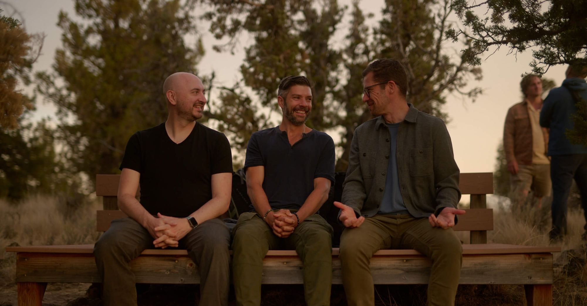Three men sitting side by side on a wooden bench outdoors
