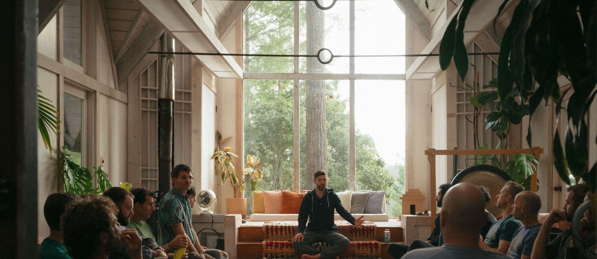 Men seated in a circle in a bright, wood-panelled hall