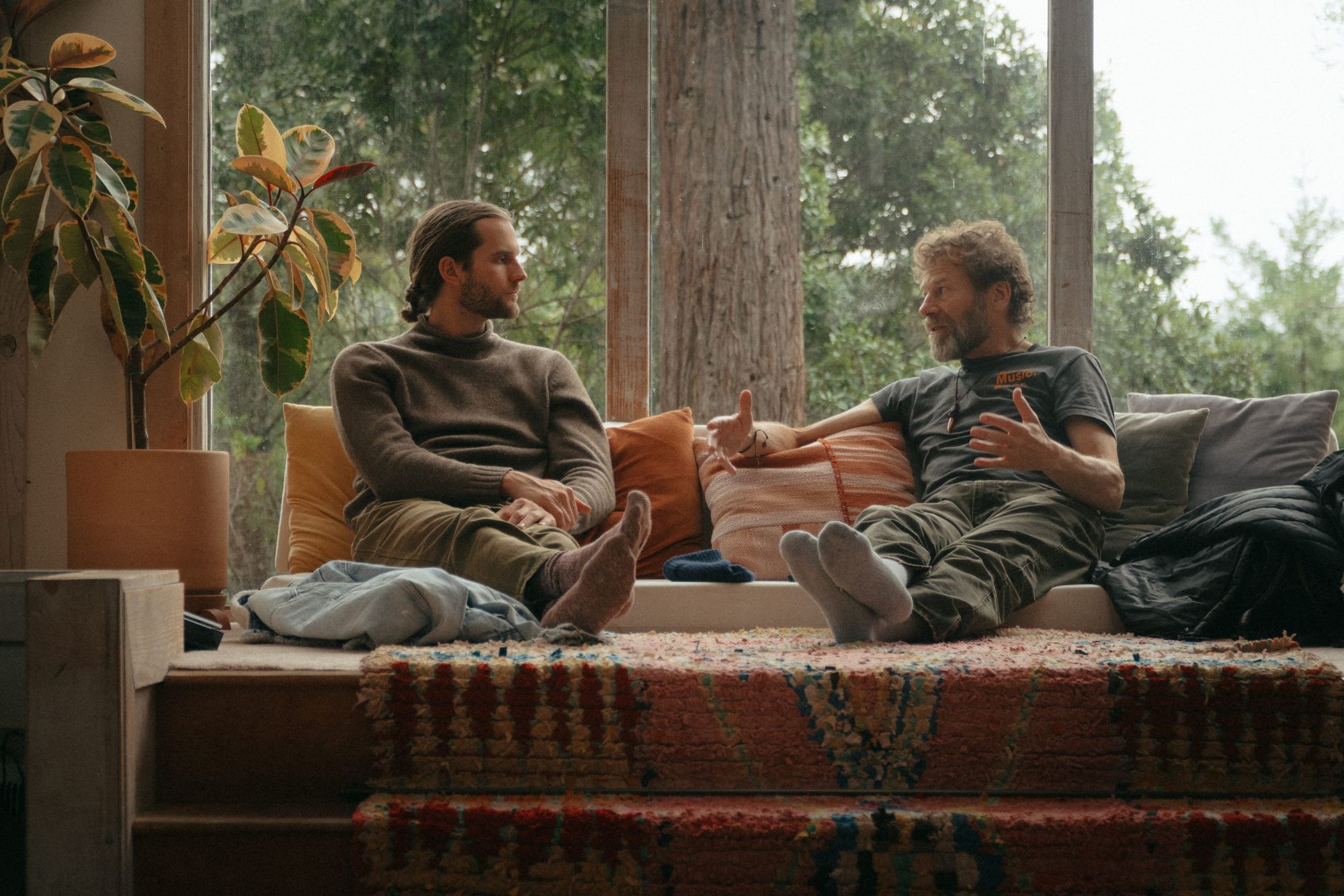 Two men in conversation on a couch in a bright, wood-framed room
